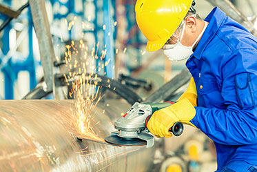 Vergrößerungsansichten für Bild: Ein Mann in Arbeitsschutzkleidung ist beim Schleifen in einem Werk zu sehen. 